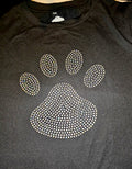 A black crewneck sweatshirt featuring a large paw print graphic embellished with sparkling rhinestones, laid flat on a dark surface.